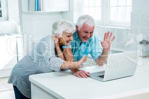 Happy senior couple gesturing while using laptop