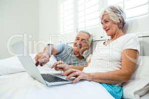 Senior man and woman using laptop on bed