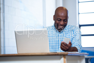 Man using mobile phone with laptop on table