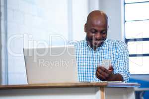 Man using mobile phone with laptop on table