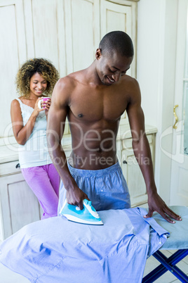 Young man ironing a shirt in kitchen