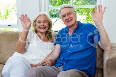 Happy senior couple waving hands while sitting at home