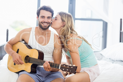 Man playing guitar while woman kissing him on cheek