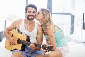 Man playing guitar while woman kissing him on cheek
