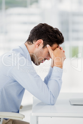 Tensed businessman sitting at table with hand on forehead