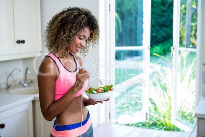 Happy woman having bowl of salad while listening to music