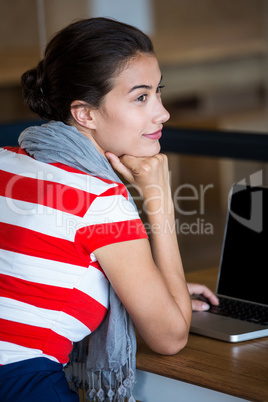 Thoughtful woman sitting at desk with laptop