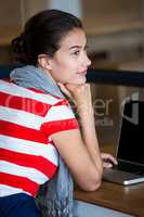 Thoughtful woman sitting at desk with laptop