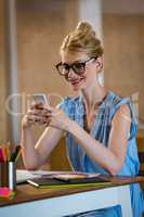 Graphic designer in office sitting at desk and text messaging on