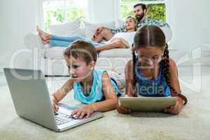 Siblings using technologies against parents relaxing on sofa