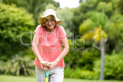 Senior woman in hat standing with rake at yard