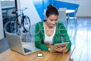 Woman using digital tablet with laptop and mobile phone on table