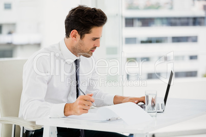 Businessman using laptop and taking notes