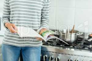 Woman reading book by stove in kitchen