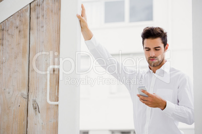 A businessman is looking his smartphone and posing his hand on a