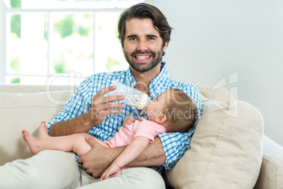 Happy man feeding milk to son while sitting on sofa