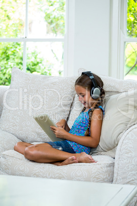 Girl using digital table while listening music against window