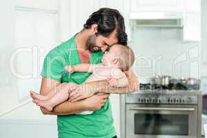 Father carrying baby boy in kitchen at home