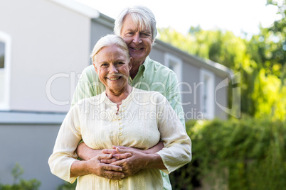 Senior couple embracing against house