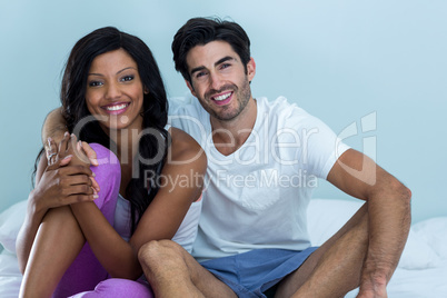 Portrait of young couple sitting on bed and smiling in bedroom