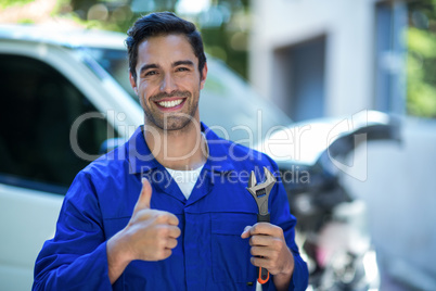 Portrait of happy mechanic with wrench showing thumbs up