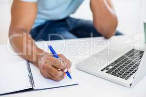 Mid section of a man with laptop writing in diary