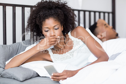 Shocked woman looking at mobile phone in bed