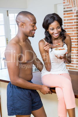 Young woman having breakfast cereal while man standing beside he