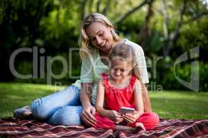 Mother looking at daughter using phone in yard