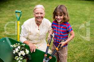 Boy with granny holding scissors over wheelbarrow at yard