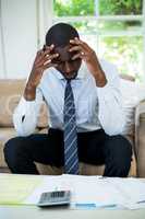 Tensed man sitting on sofa with bills and calculator