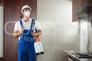 Front view of pest worker spraying in kitchen