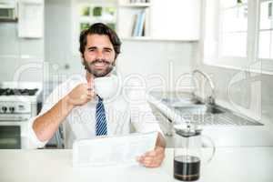 Confident businessman drinking coffee while reading newspaper