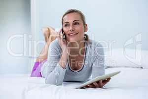 Thoughtful woman holding digital tablet while talking on phone o
