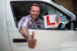 Young man gesturing thumbs up holding a learner driver sign