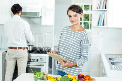 Woman using digital tablet while man preparing food