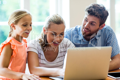 Father looking at mother and daughter using laptop