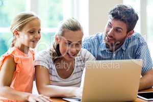 Father looking at mother and daughter using laptop