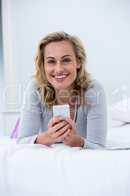 Young woman with mobile phone lying on bed