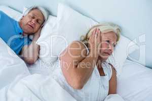 Senior woman blocking ears while man snoring