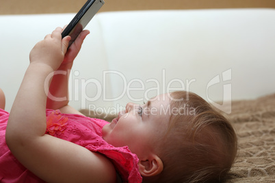 little cute girl lying on the couch and playing with a smartphone