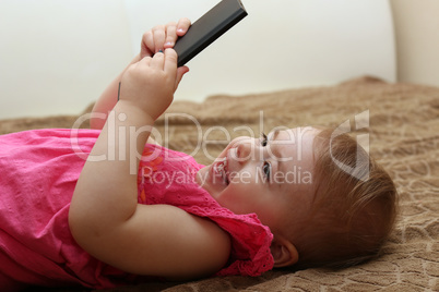 little smiling child playing with your smartphone lying on a sofa