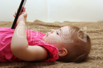 little cute girl lying on the couch and playing with a smartphone