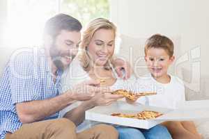 Parents and child sitting on sofa and having pizza