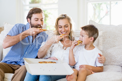 Parents and child sitting on sofa and having pizza