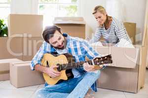 Man playing a guitar while woman unpackaging cardboard boxes in