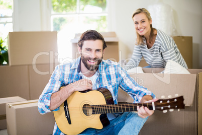 Man playing a guitar while woman unpackaging cardboard boxes in