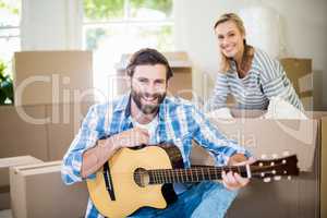 Man playing a guitar while woman unpackaging cardboard boxes in