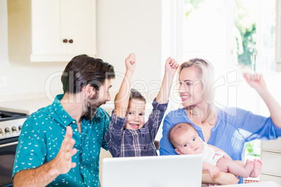 Excited parents and kids using laptop in kitchen