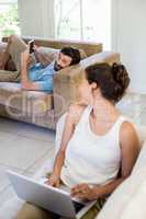 Young couple using laptop and mobile phone in living room